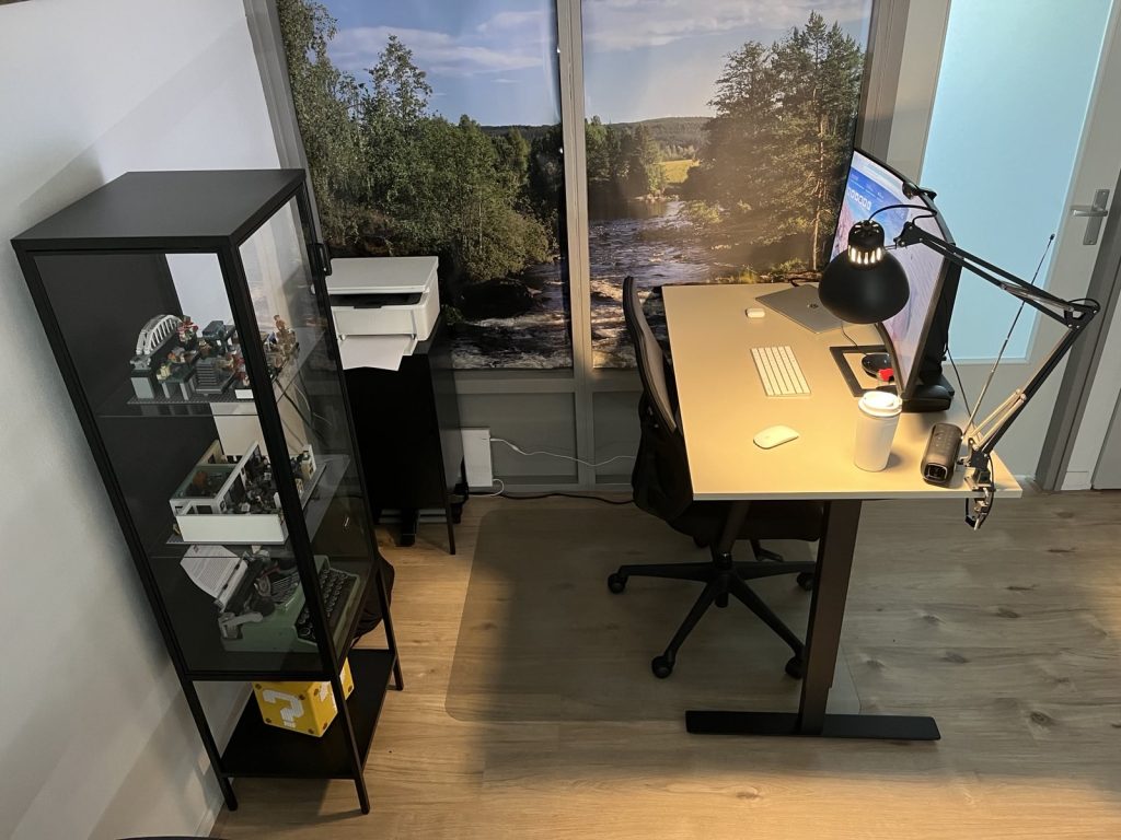 Mijn werkplek vanaf de zijkant, met op de achtergrond een poster van een foto die in Zweden is gemaakt. Op de foto staat een wild stromend riviertje en veel groen.